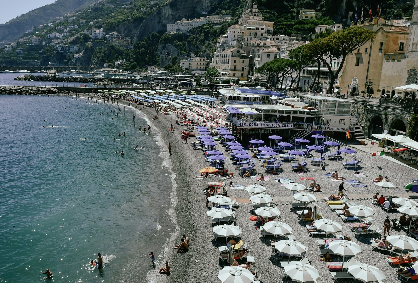 Crowded beach with umbrellas below hillside town